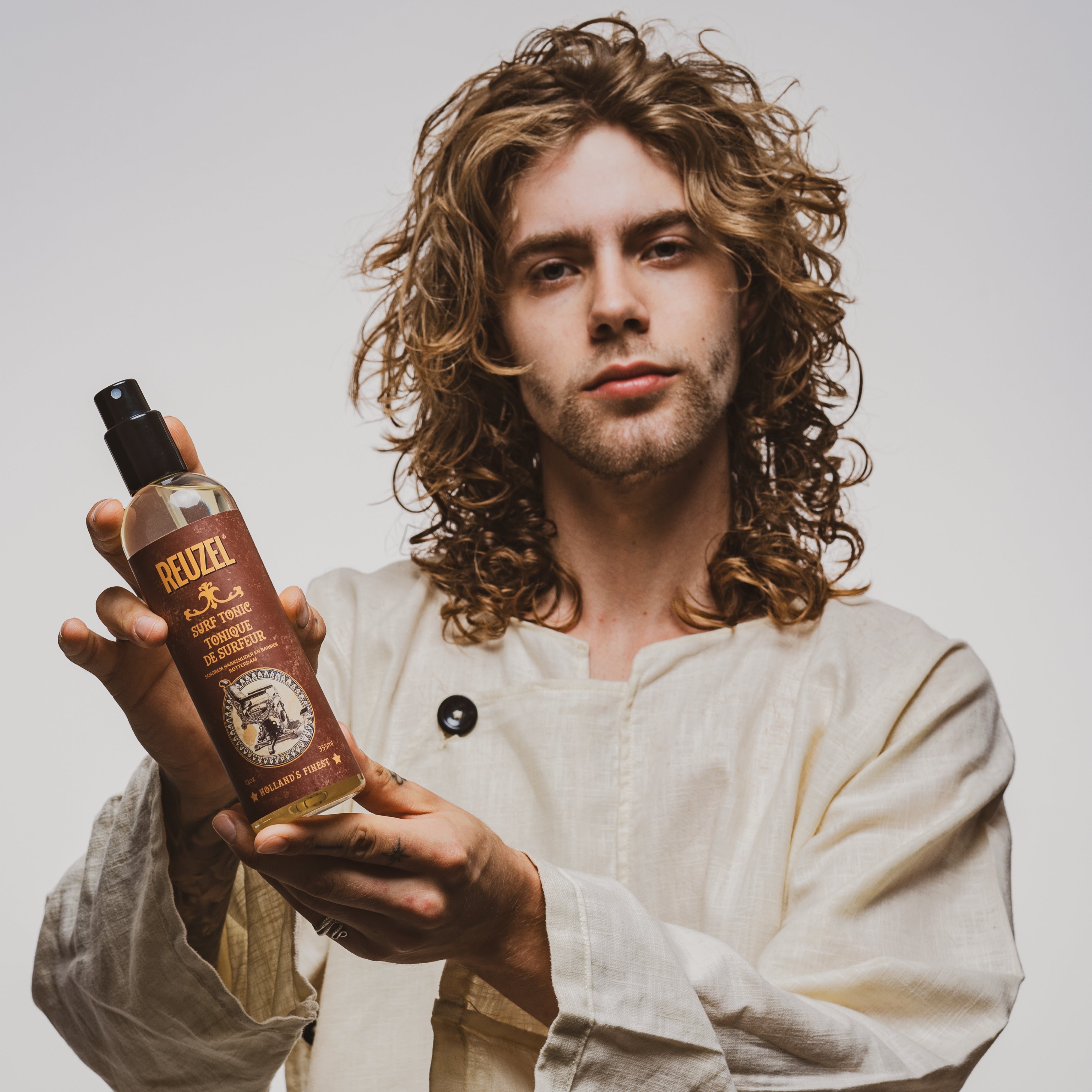 Reuzel Surf Tonic salt spray hair tonic in a clear spray bottle with a black cap, designed for textured, beachy hairstyles.