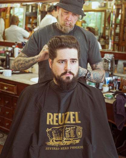 Reuzel X Liquid Death Severed Head barber cape with bold graphic design, made for professional grooming and barber use.